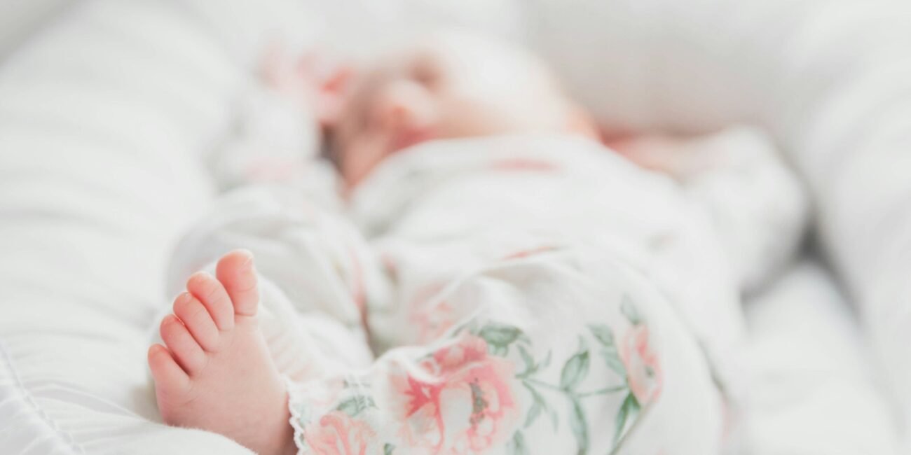 baby in white and red floral onesie lying on bed