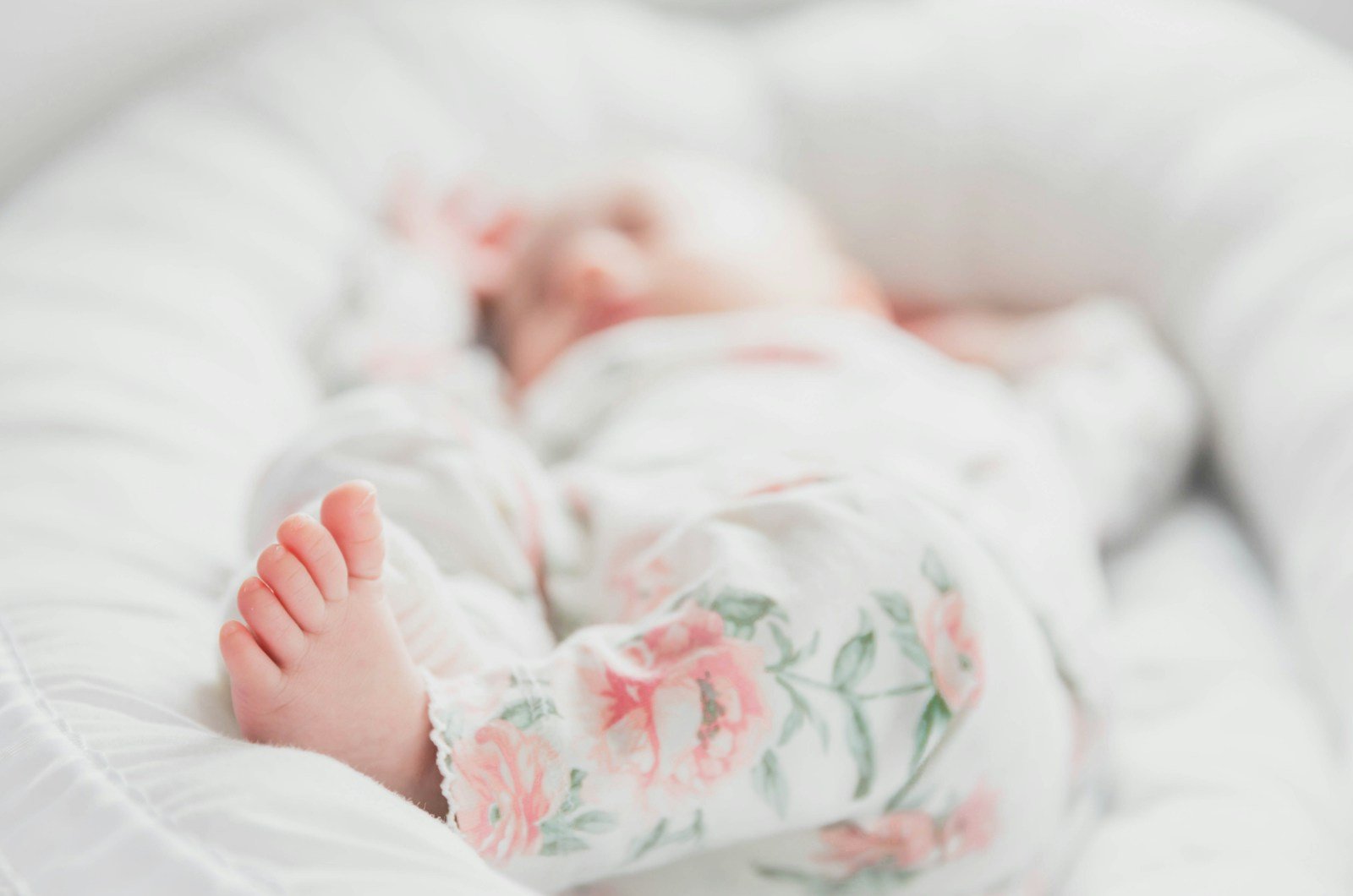 baby in white and red floral onesie lying on bed