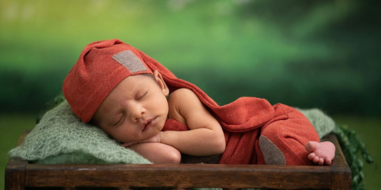 baby in red blanket lying on green textile