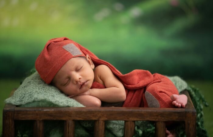 baby in red blanket lying on green textile