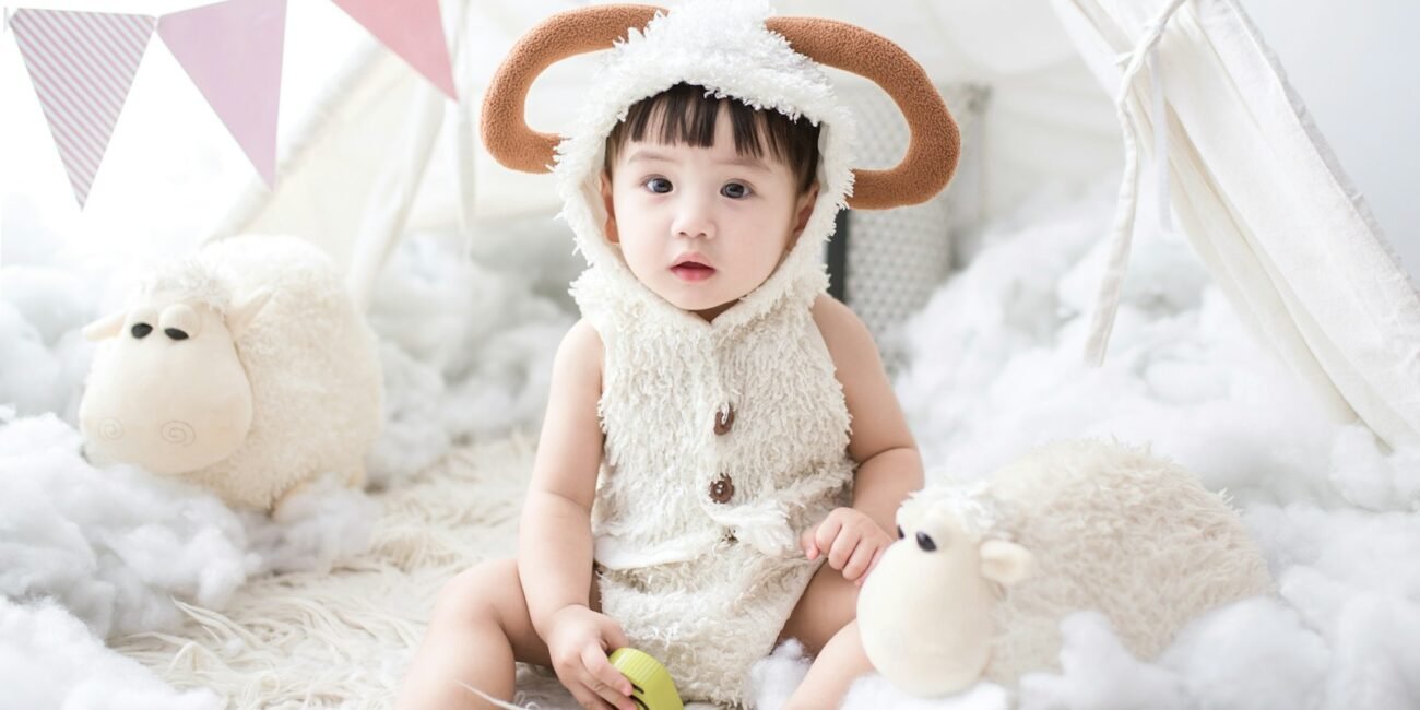 baby sitting beside white sheep plush toy