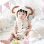 baby sitting beside white sheep plush toy