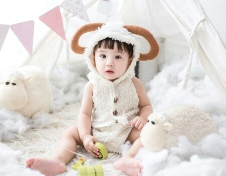 baby sitting beside white sheep plush toy